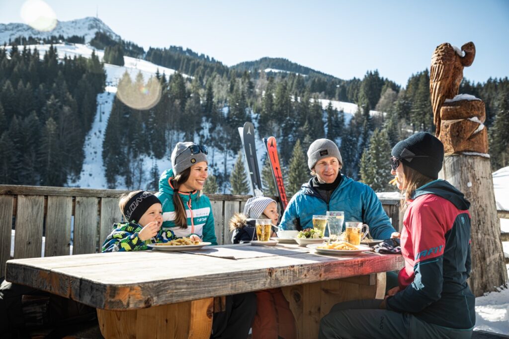 Family enjoying food and drink on a mountain with skis in the background