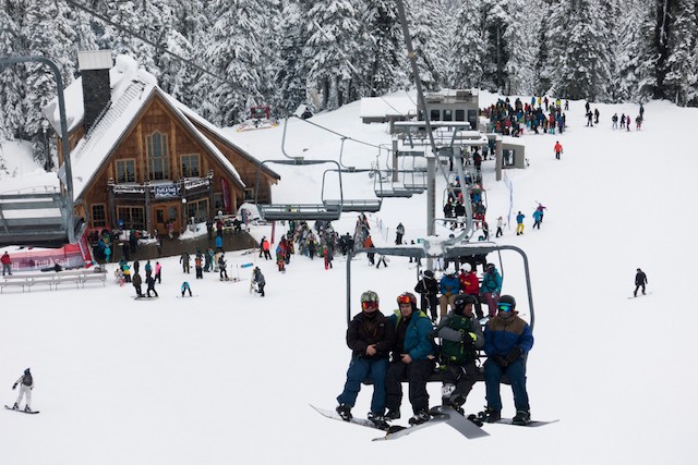 Skiiers and snowboarders ride on a chairlift above the snowy Mount Baker